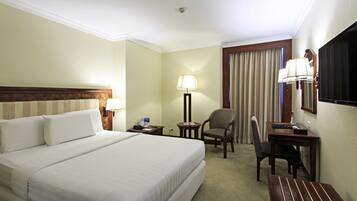 A hotel room with a large bed, two chairs, a desk, a lamp, and a window with curtains.