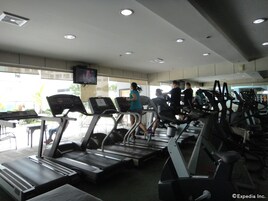 Un gimnasio con cintas de correr, un televisor montado en la pared y ventanas amplias que dejan entrar luz natural.