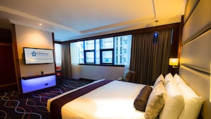 Hotelkamer met een groot bed, een flatscreen televisie aan de muur, een raam met gordijnen en een vloerkleed met een geometrisch patroon.