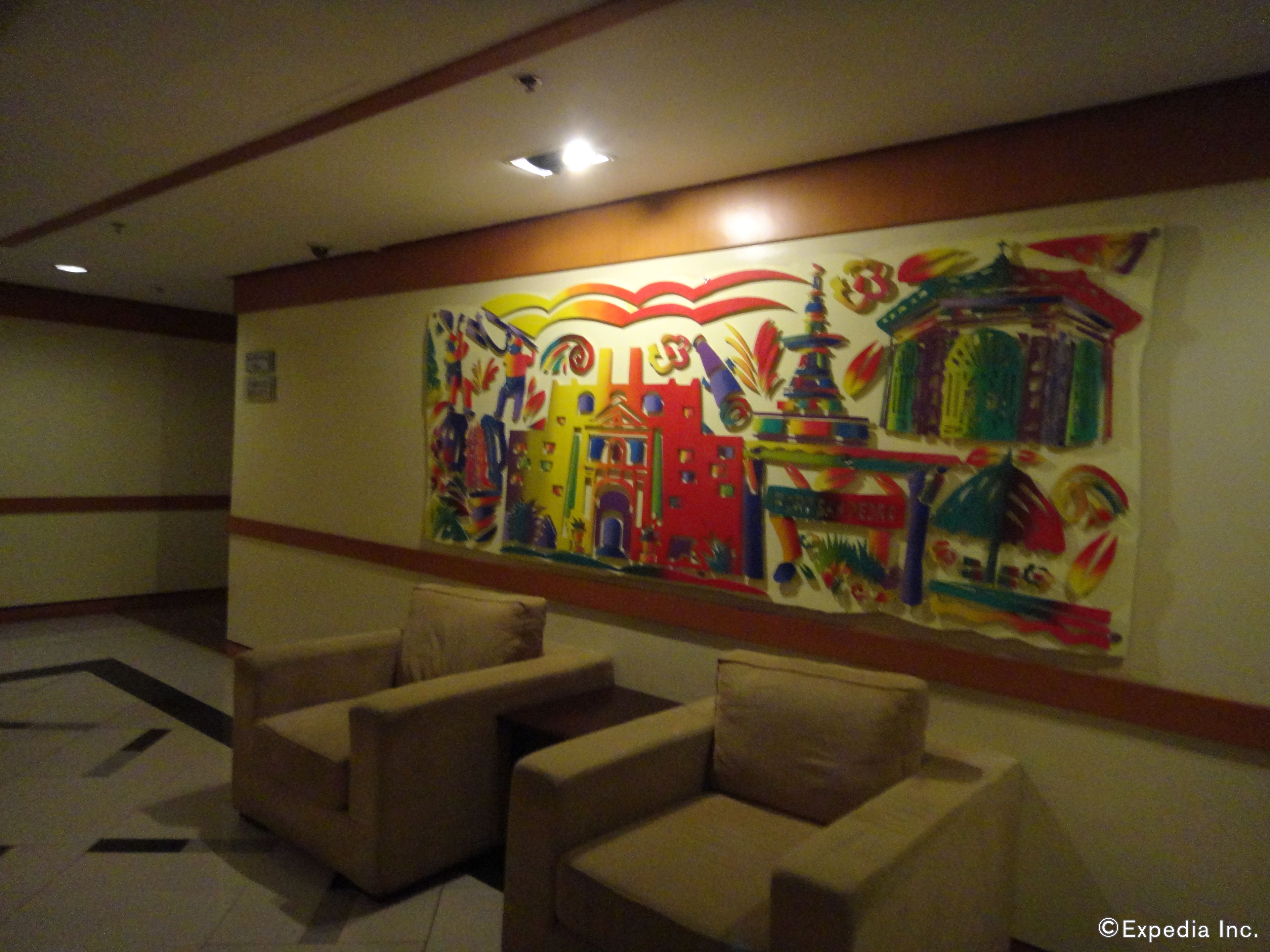 A lobby with a colorful mural on the wall, beige armchairs, and a tiled floor.
