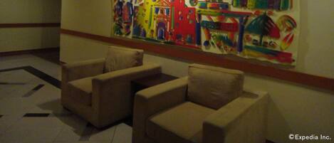 A lobby with a colorful mural on the wall, beige armchairs, and a tiled floor.