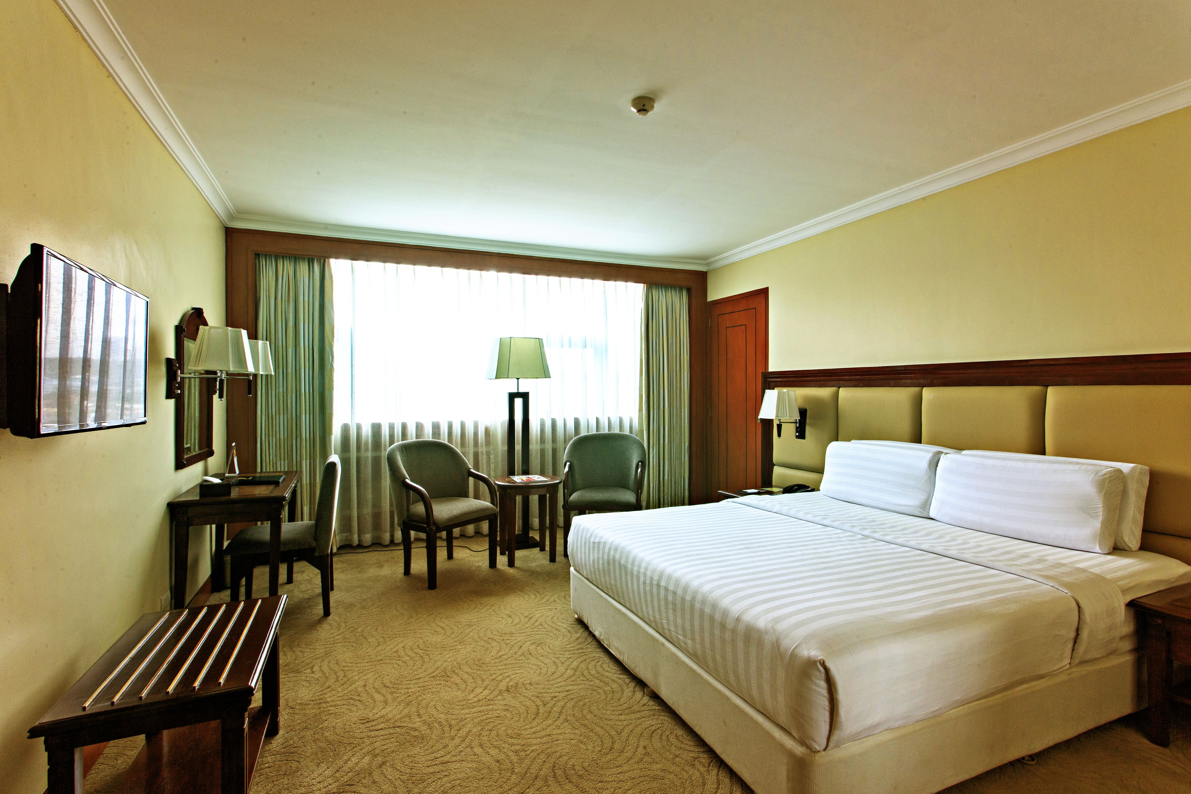 A hotel room with a large bed, two chairs, a small table, and a desk with a lamp.