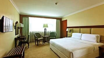 A hotel room with a large bed, two chairs, a small table, and a desk with a lamp.