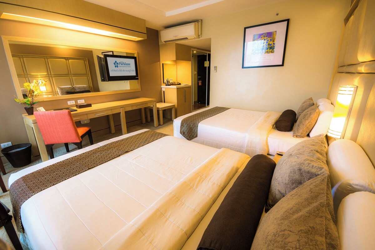 Une chambre d’hôtel avec deux lits, un bureau, une chaise, une petite table et un tableau encadré au mur.