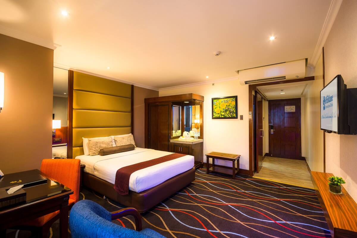 Habitación de hotel con una cama grande, un escritorio, una silla, una mesita, un televisor y una puerta que da al pasillo.