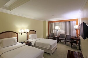 A hotel room with two beds, a desk, a chair, and a television.