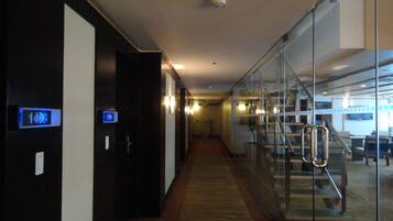 Een hotelgang met een digitaal bord waarop kamer 1408 staat, een glazen scheidingswand en een trap die naar een hoger niveau leidt.