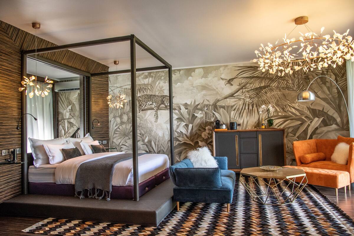 Un dormitorio moderno con una cama con dosel, un sillón azul, un sofá naranja y una alfombra estampada.