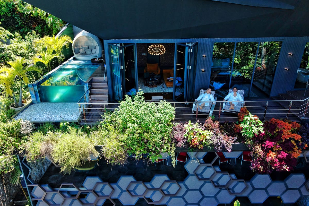 Una casa moderna con piscina, mobiliario exterior y abundante vegetación.