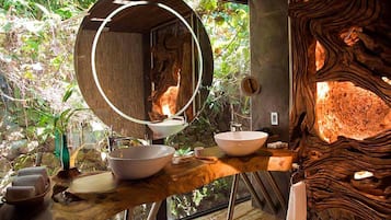 Relax in this serene bathroom with a large mirror, sink, and wooden vanity, surrounded by lush greenery and a natural stone wall.