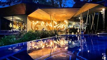 Un área de piscina exterior con superficie reflectante, rodeada de zonas de estar y un edificio de diseño espiral único.
