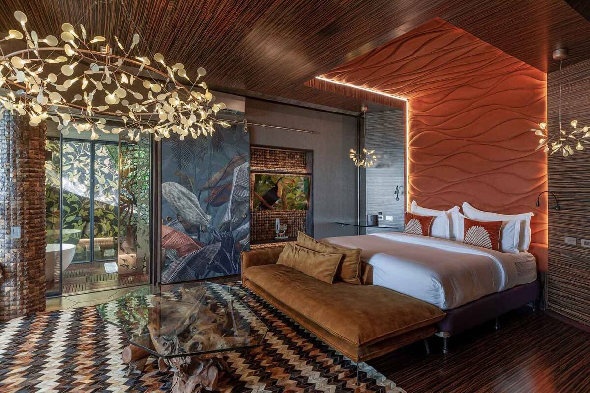 Un dormitorio moderno con una cama grande, un rincón de estar con paredes de cristal y una pared con una textura original.