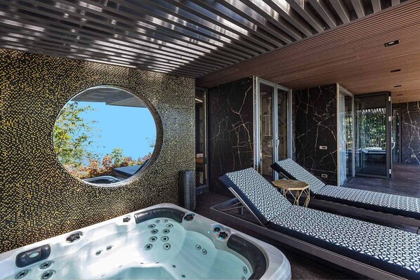 A modern spa area with a hot tub, lounge chairs, and a large circular mirror reflecting the outdoors.