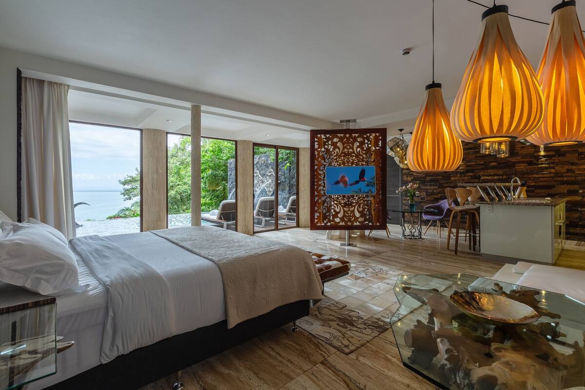 Habitación de hotel moderna con una cama grande, una mesa de centro de cristal y vistas al mar.