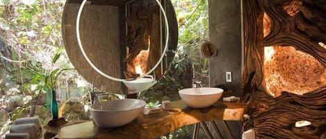 A bathroom with a wooden vanity, a round mirror, and a stone wall.