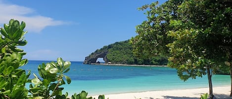 Una playa con agua turquesa cristalina, una orilla arenosa y abundante vegetación.