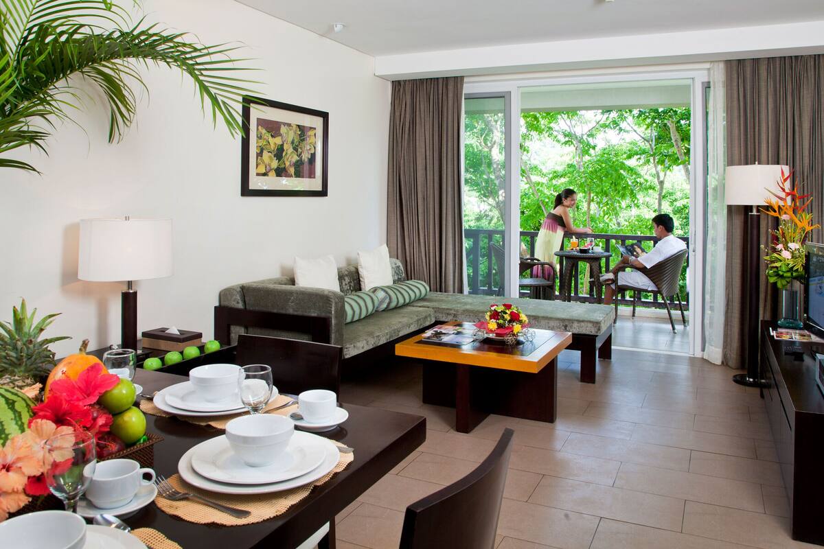Une chambre d’hôtel comprenant un coin repas, un canapé, un balcon avec vue sur les arbres et une télévision.