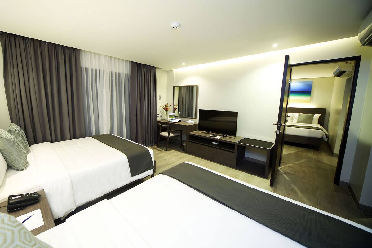 Une chambre d’hôtel avec deux lits, un bureau, une chaise, une télévision et une salle de bain visible à travers une porte ouverte.