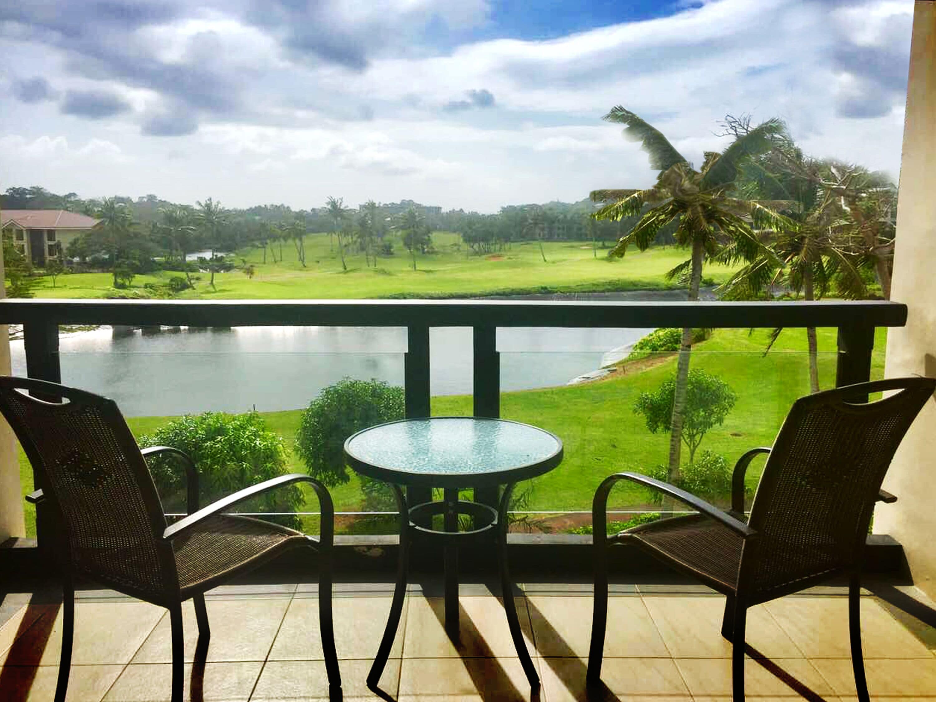A balcony with two chairs and a small table, overlooking a golf course and a body of water.