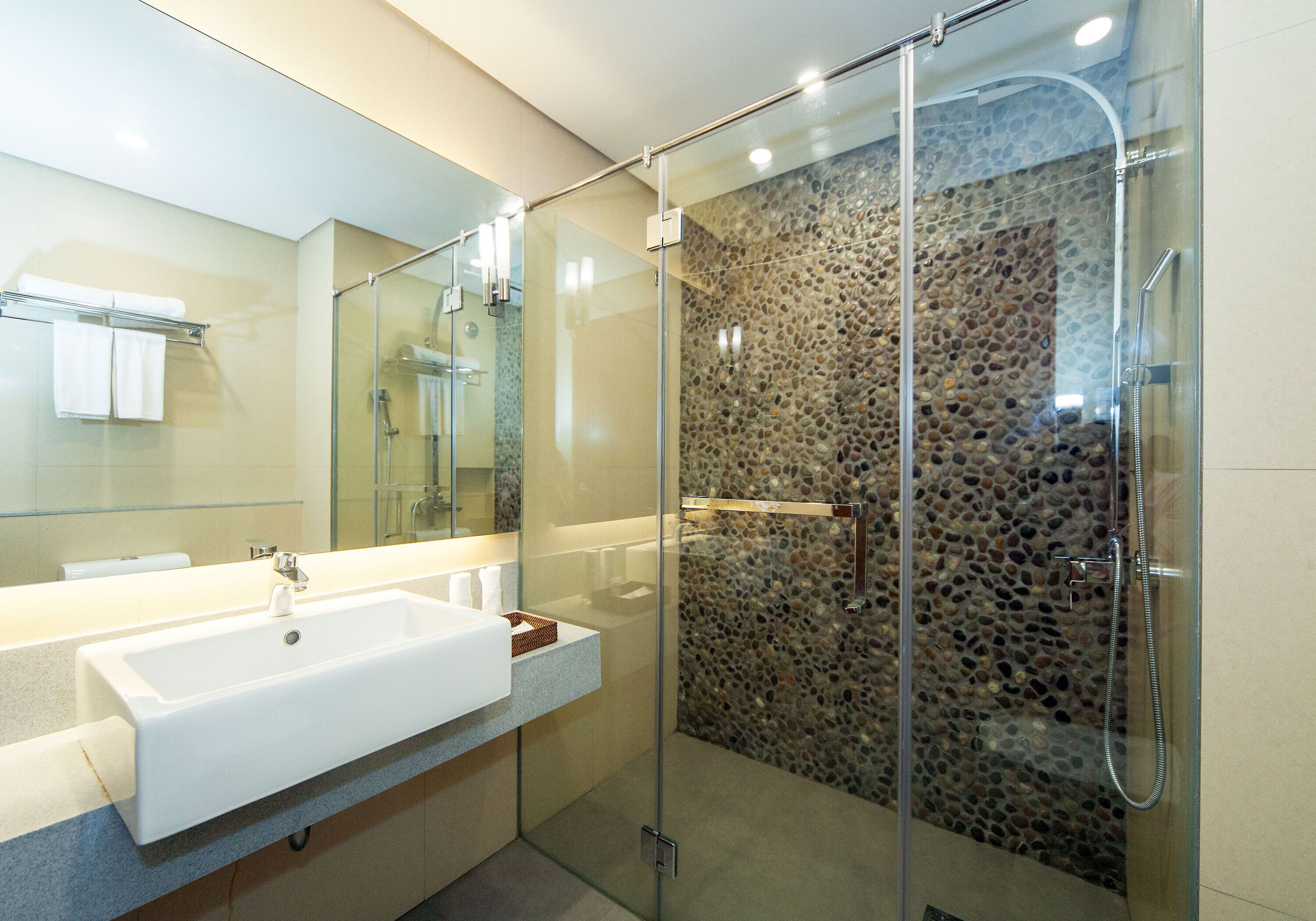 A modern bathroom with a glass-enclosed shower, a white sink, and a stone-textured wall.