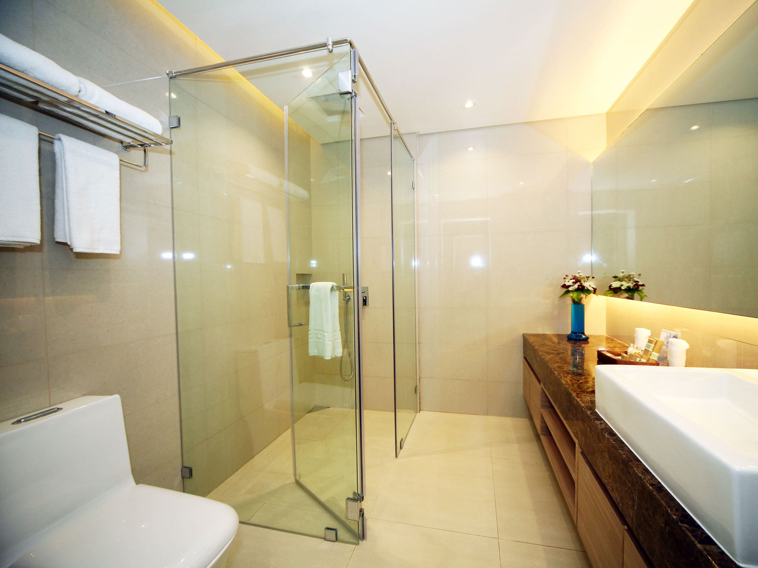 Un baño moderno con ducha envuelta en vidrio, un lavamanos blanco y un mueble de tocador de madera.
