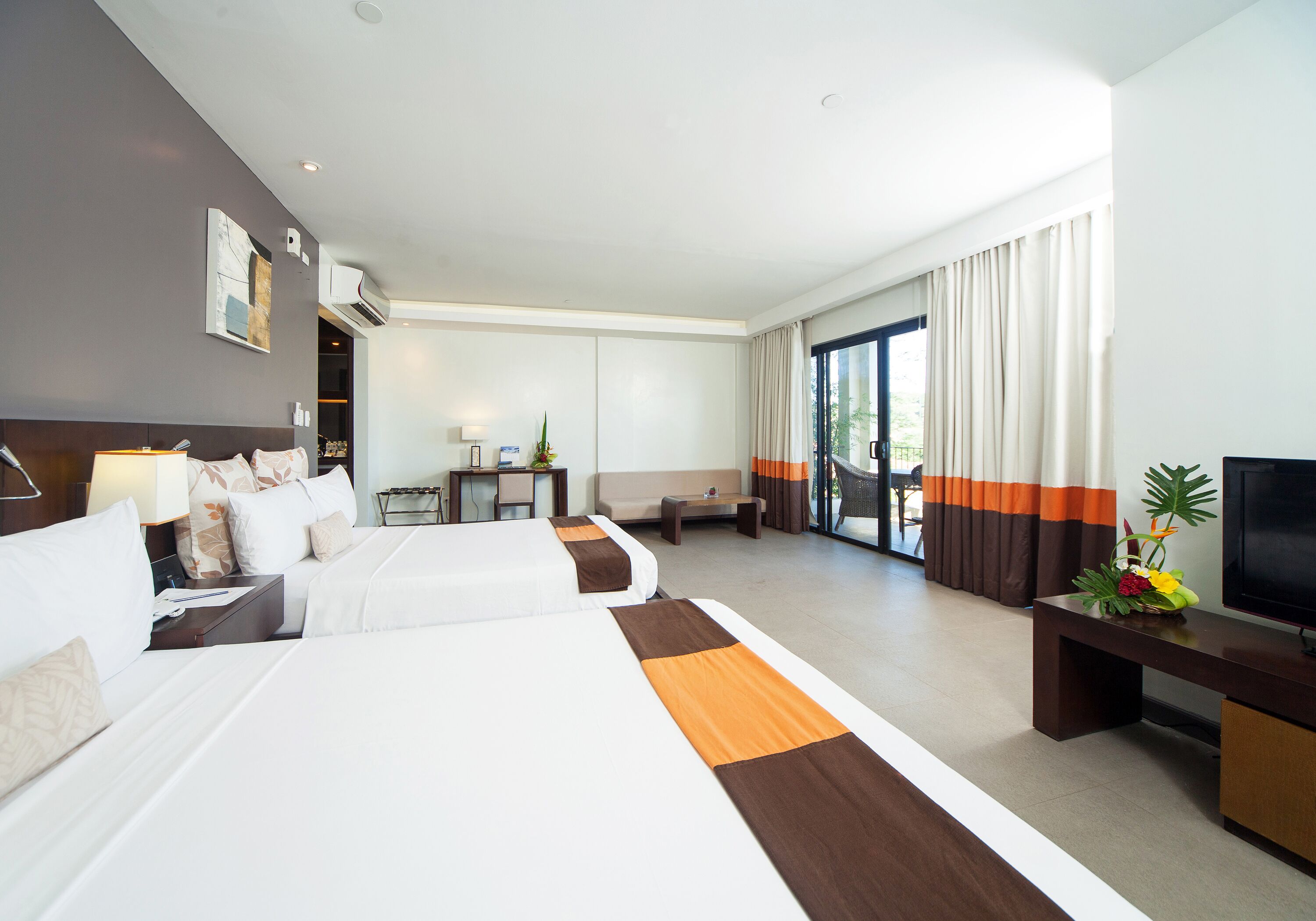 Une chambre d’hôtel avec deux lits, un canapé, une télévision et un balcon avec des rideaux.
