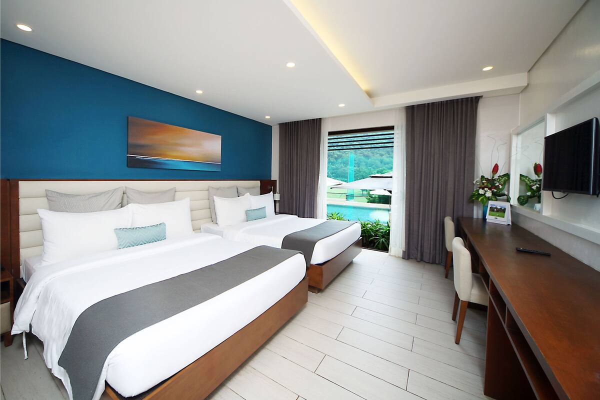 Une chambre d’hôtel moderne avec deux lits, un bureau et une grande fenêtre donnant sur une piscine.