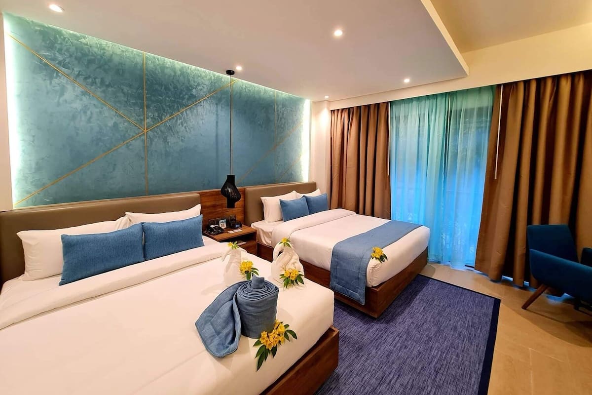 Une chambre d’hôtel moderne avec deux lits, une grande fenêtre avec des rideaux et un mur d’accent bleu.