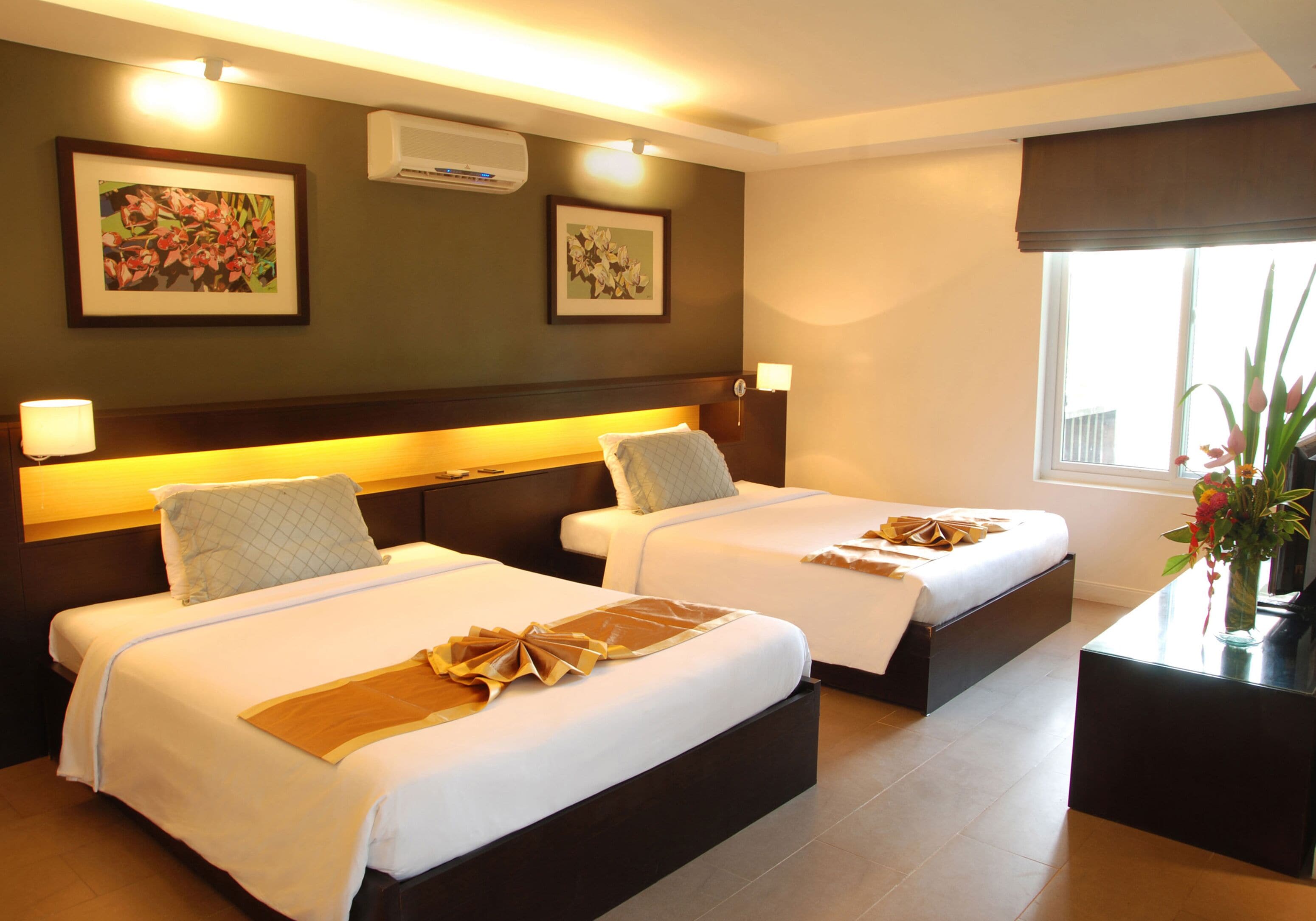 A hotel room with two beds, a nightstand, a desk, and a window with a view.