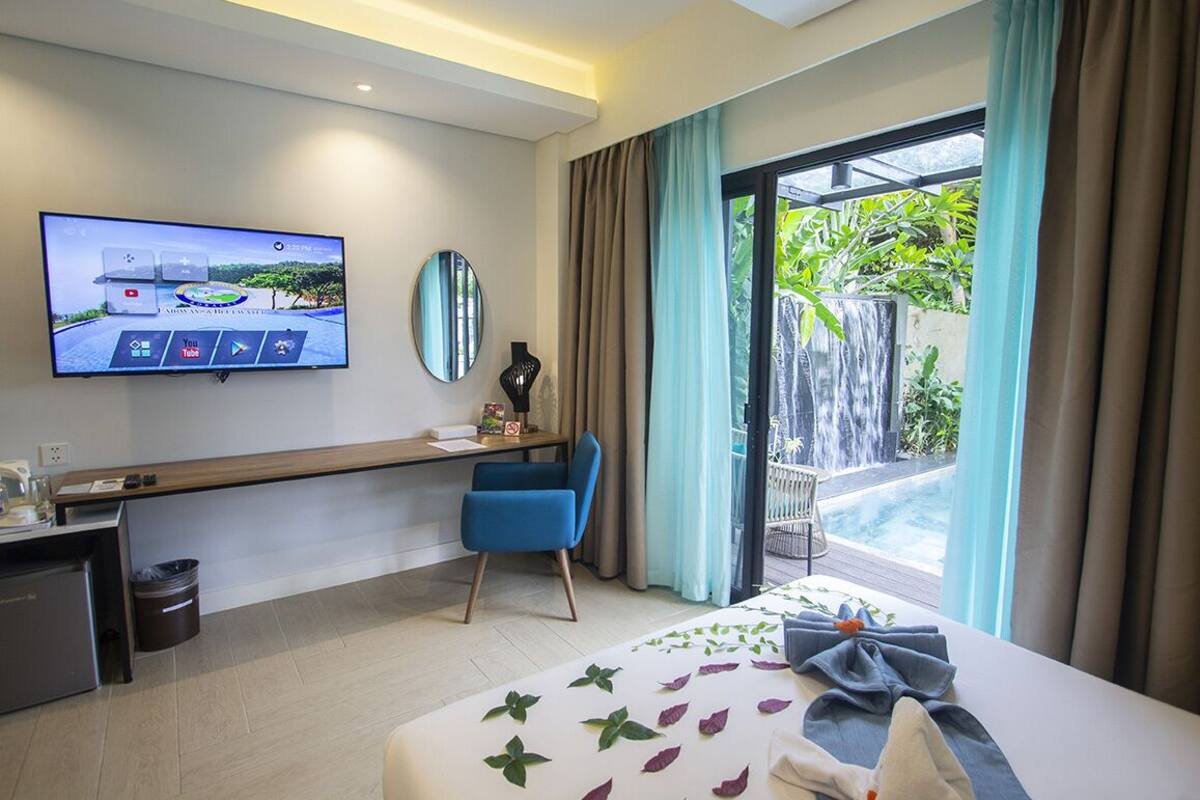 Une chambre d’hôtel équipée d’un lit, d’un bureau, d’une télévision et offrant une vue sur une piscine et un espace verdoyant.