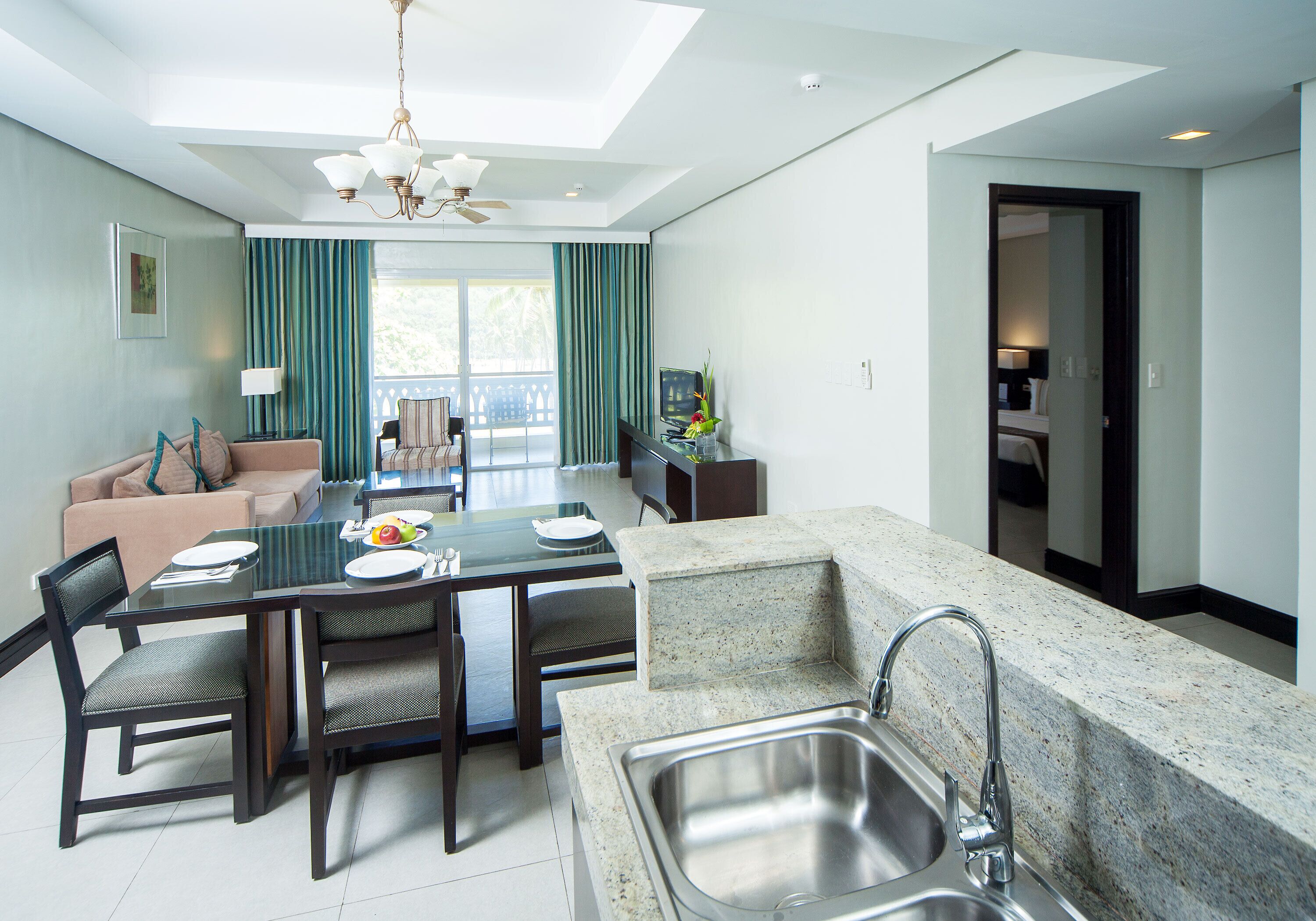 A modern kitchen with granite countertops, a stainless steel sink, and a dining area with a glass table and chairs.