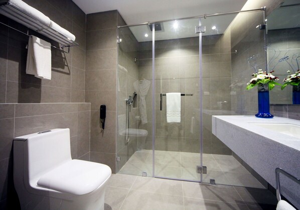 Une salle de bain moderne avec une douche à parois de verre, des toilettes blanches et un meuble-lavabo agrémenté d’un vase bleu.
