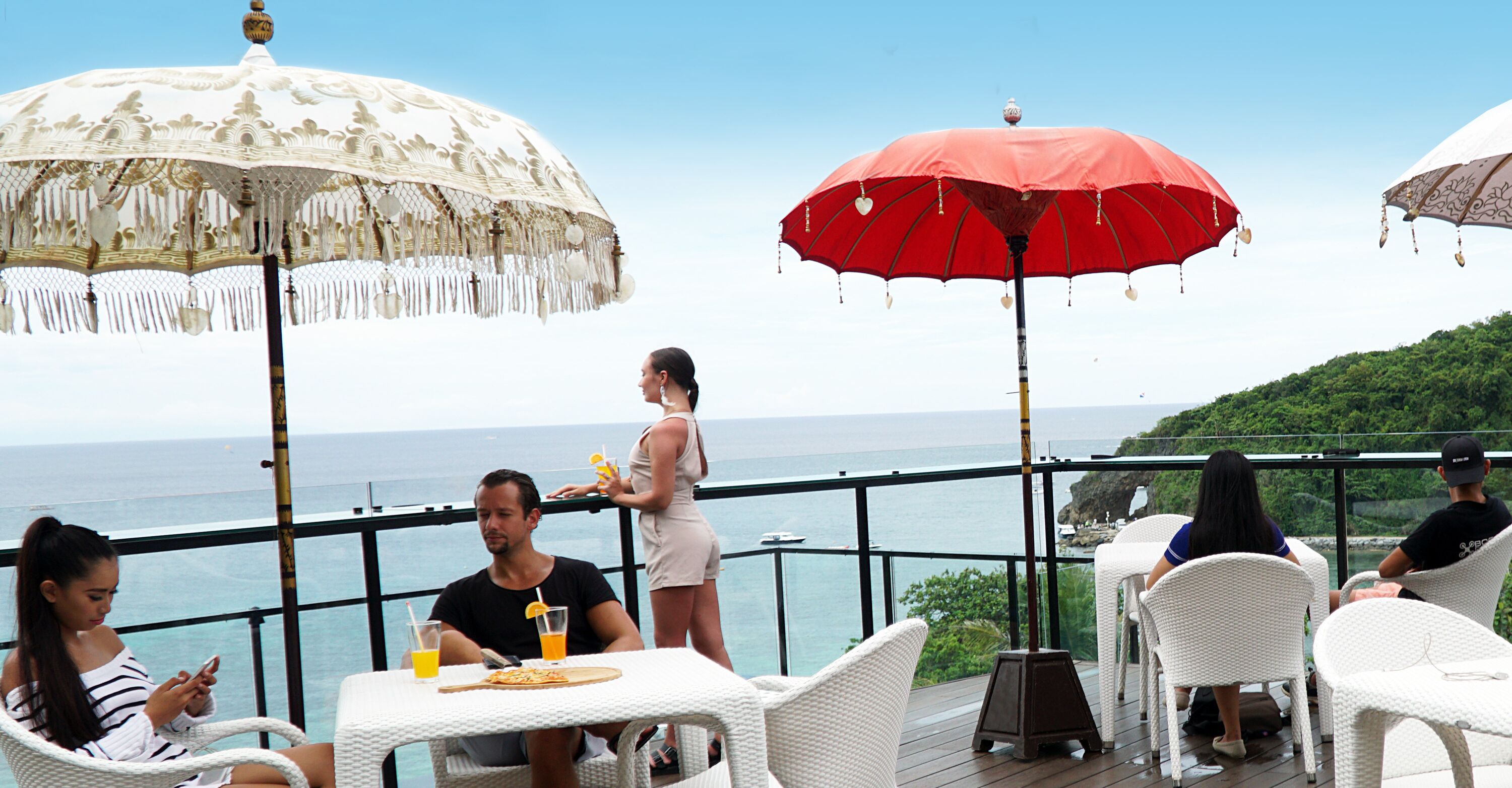 A terrace with white wicker furniture, a table with drinks, and two large umbrellas providing shade.