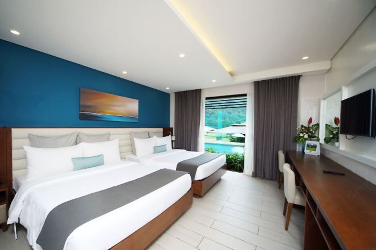 Habitación de hotel con dos camas, un escritorio, un televisor y una ventana con cortinas.