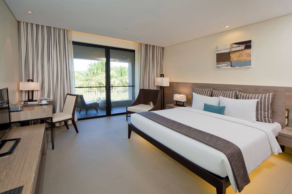 Une chambre d’hôtel moderne dotée d’un grand lit, d’un bureau avec un ordinateur, d’une chaise et d’un balcon avec des rideaux.