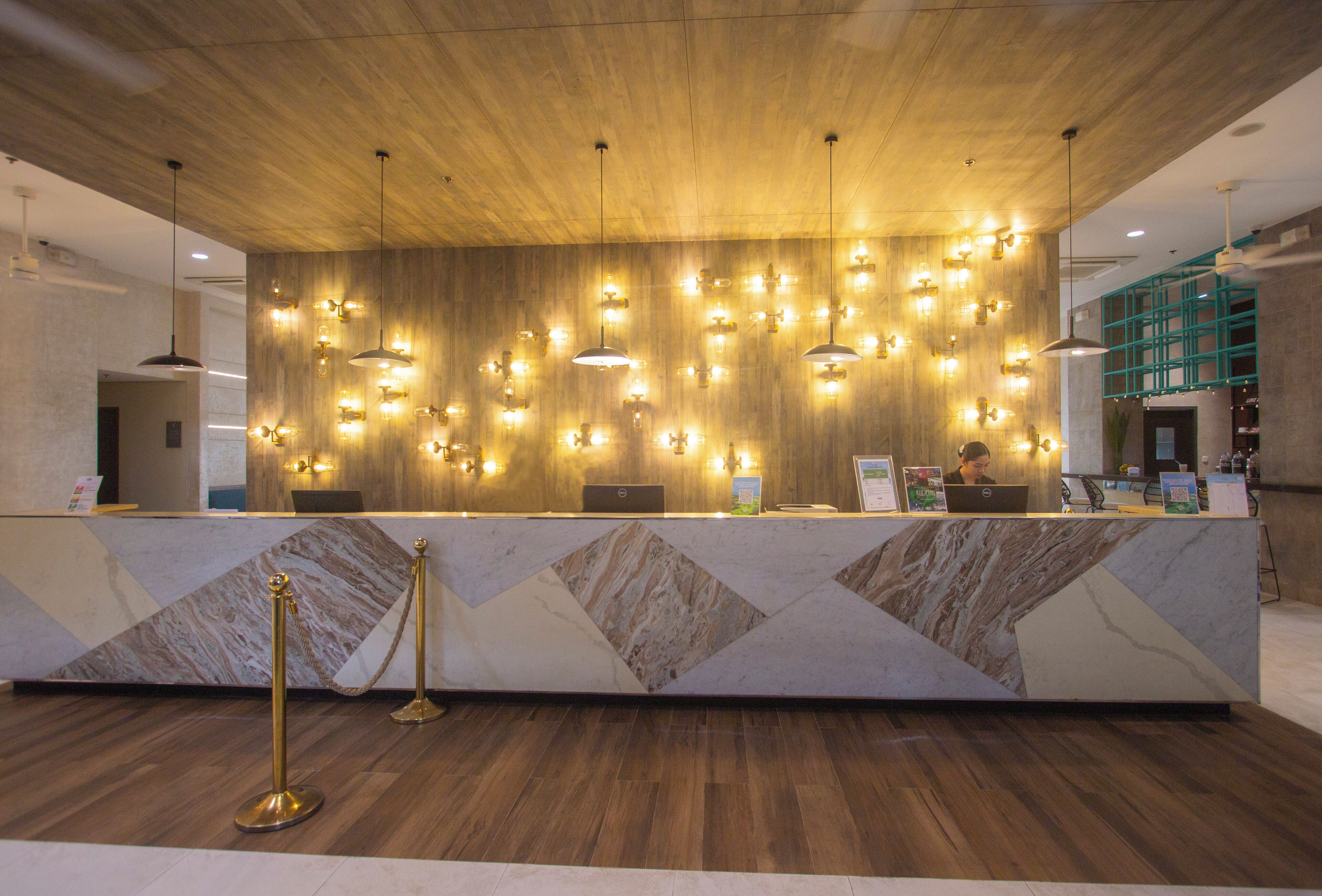 A reception desk with a marble design, multiple pendant lights, and a laptop on the counter.