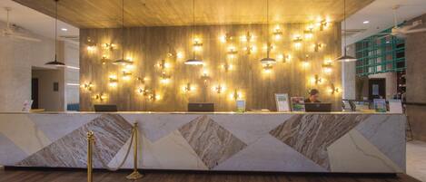 A reception desk with a marble design, multiple pendant lights, and a laptop on the counter.