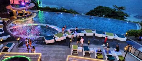 A pool area with lounge chairs and a neon sign indicating 'Happy Hour'.