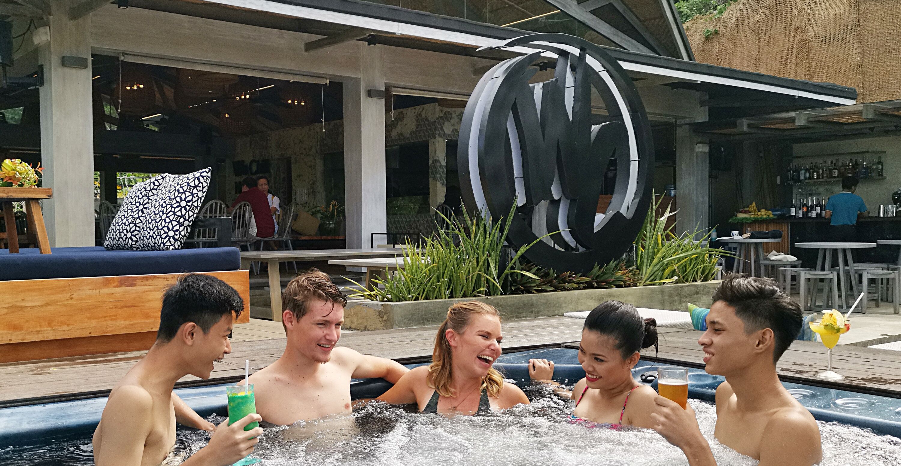 Een groep mensen in een jacuzzi, met een bar op de achtergrond.