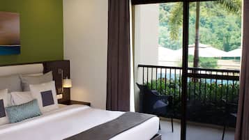 A hotel room with a large bed, a balcony with a view of a pool and greenery.