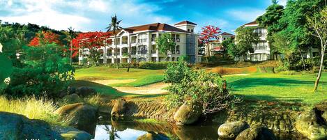 Villas by a golf course with a pond, rocks, and lush greenery.