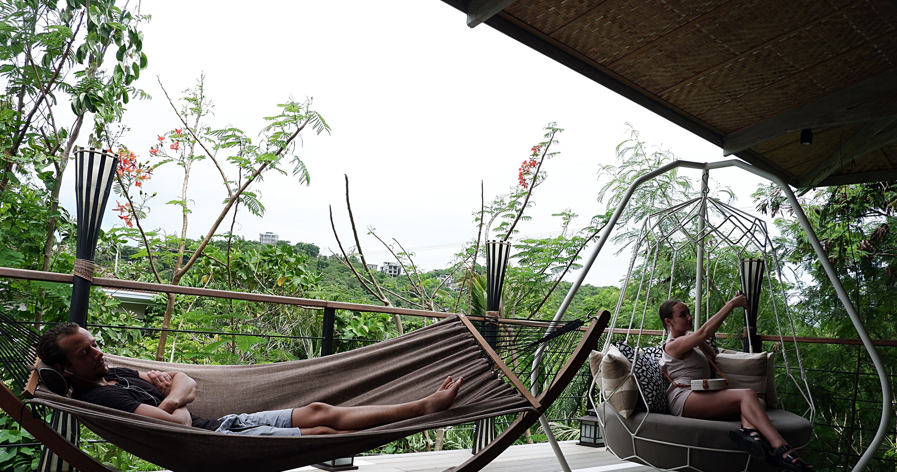 Two people relaxing on hammocks in an outdoor setting with lush greenery and a wooden deck.