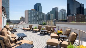 A rooftop deck with outdoor furniture, a city skyline in the background, and a building with a sign that reads "The Cornelius". - The Belltown Inn (Seattle)