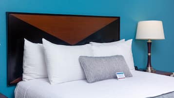 A hotel room with a large bed, white bedding, a wooden headboard, a bedside lamp, and a sign on the bed.