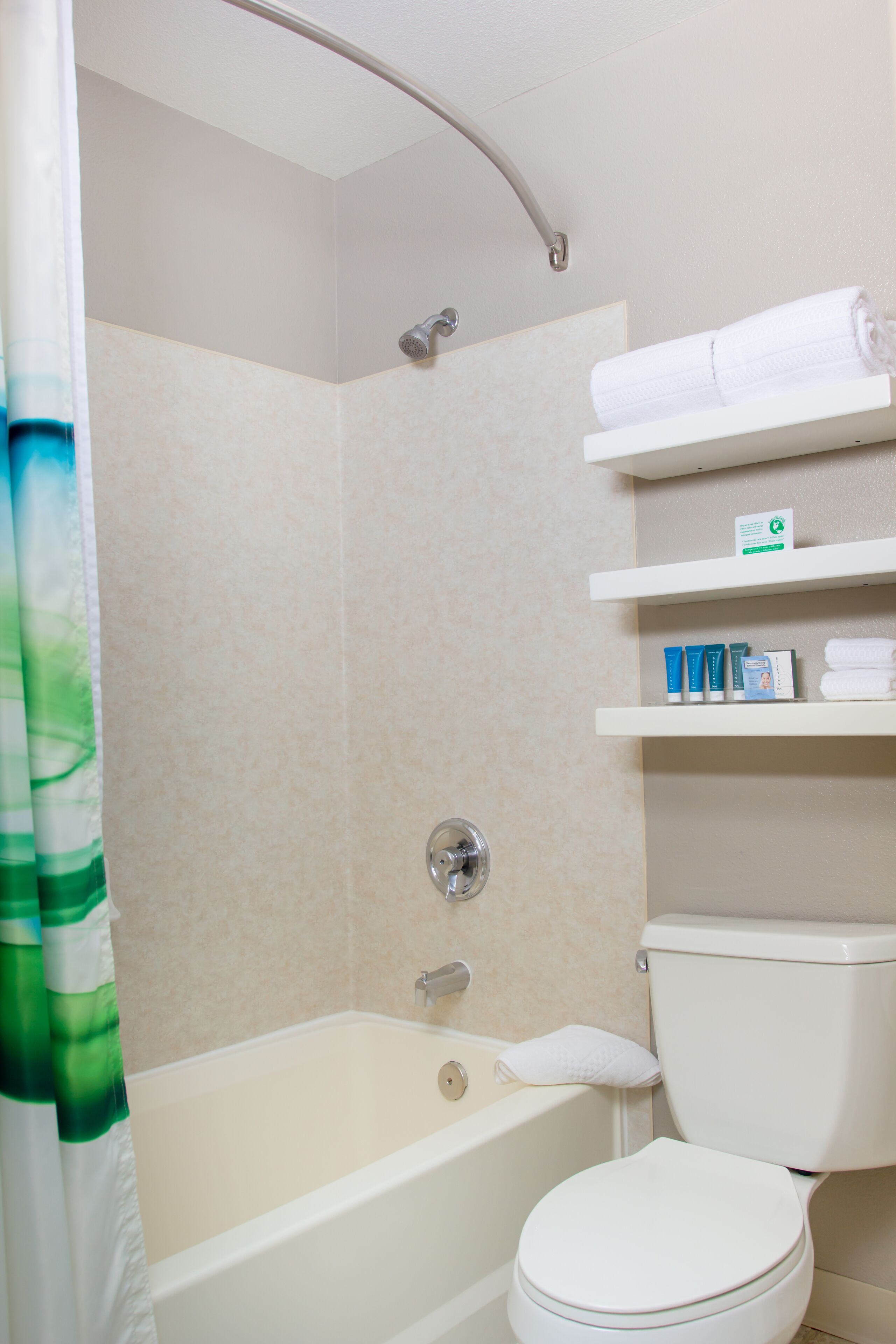 A bathroom with a bathtub, toilet, shower, and shelves with toiletries.
