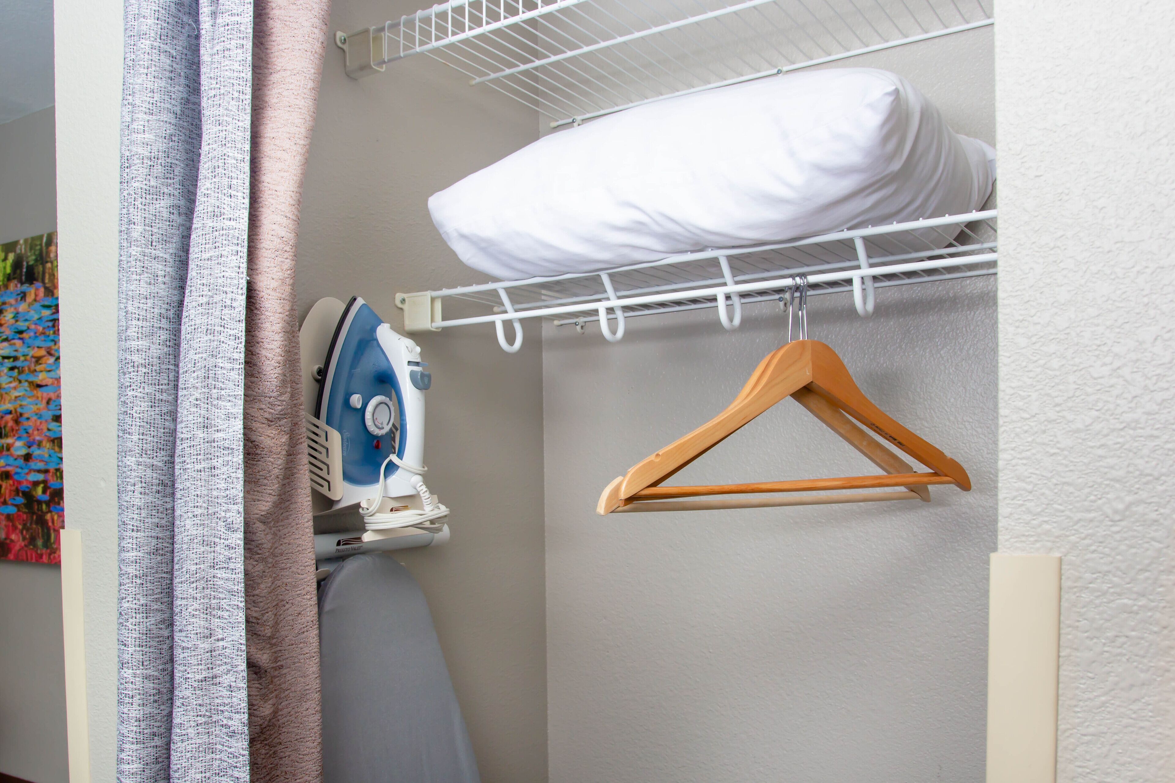 Een netjes ingerichte wasruimte met een ophangrek, een strijkijzer en een houten hanger.