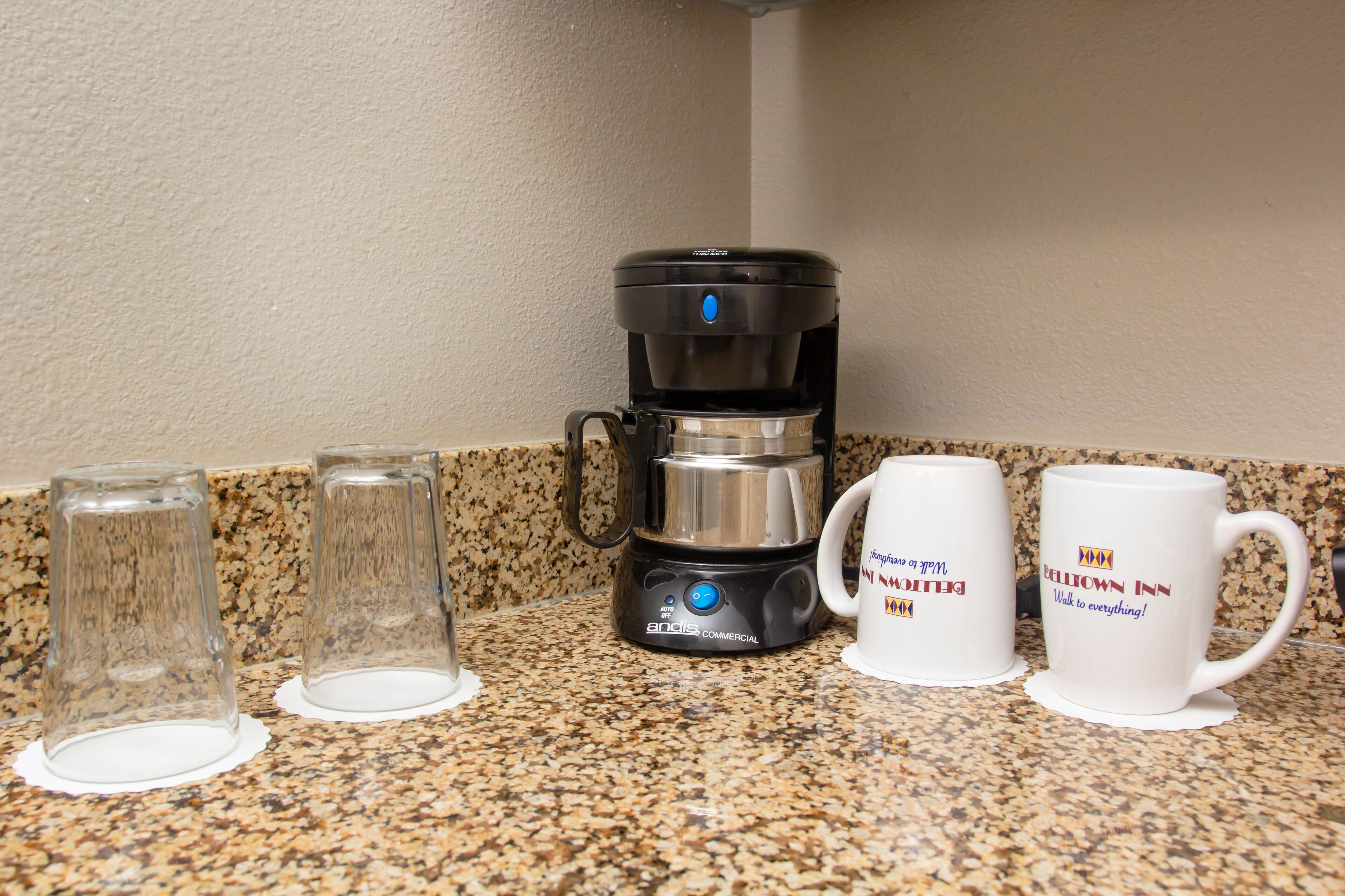 A coffee maker, two glasses, and two mugs on a granite countertop.