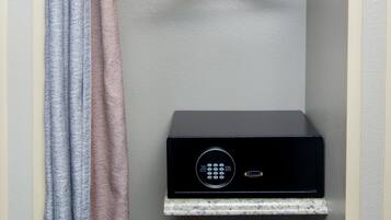 A small, enclosed room with a white shelf, a hanging wooden hanger, a white pillow, and a black electronic device on a marble shelf.