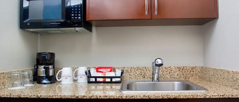 Una cocina con microondas, cafetera y máquina de café. Hay un lavabo y una encimera con escurreplatos.