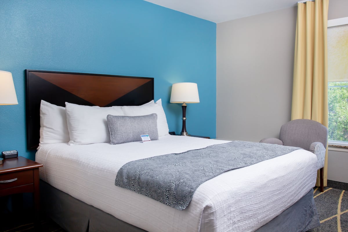 A hotel room with a large bed, two bedside lamps, a chair, and a window with curtains.